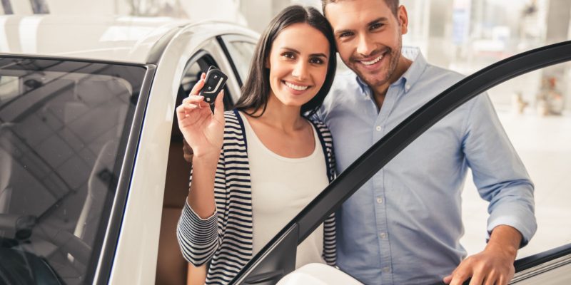 Visiting car dealership. Beautiful couple is holding a key of their new car, looking at camera and smiling