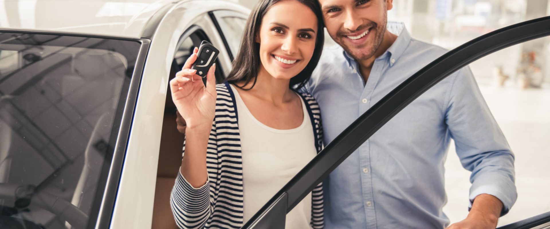 Visiting car dealership. Beautiful couple is holding a key of their new car, looking at camera and smiling