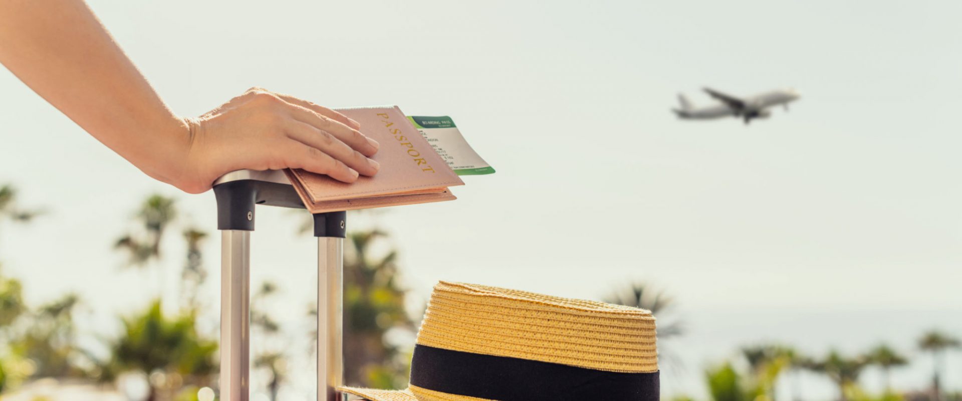 Woman with pink suitcase and passport with boarding pass standing on passengers ladder of airplane opposite sea with palm trees. Tourism concept